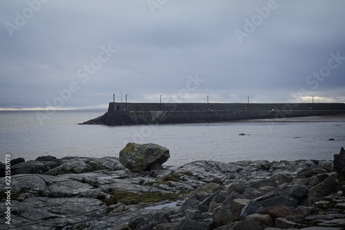 A moody view of a pier with a rocky foreground.