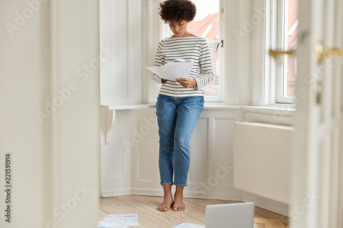 Full length shot of smart economist studies financial report, examines abstract of record, thinks how accelarte economic growth, wants to accomodate with loan and accomplish her ends. Business concept photo