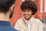 Back view of unrecognizable man meets accidentally on street old friend, have friendly conversation, discuss latest news and personal life. Happy curly dark skinned girl glad to see her groupmate