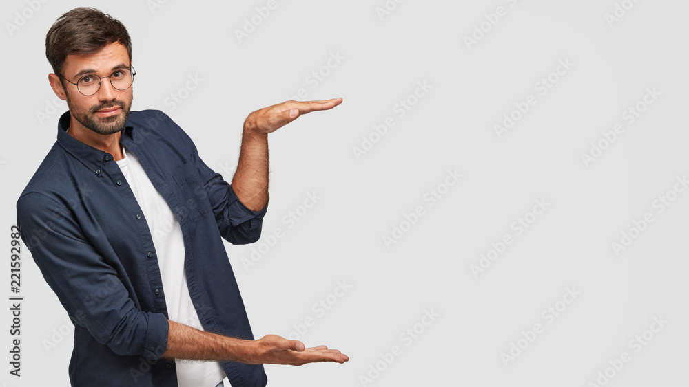 Horizontal shot of handsome Caucasian man with bristle, shows height of something with both hands, pretends holding item or thing, demonstrates size, dressed in casual outfit, isolated on white Horizontal shot of handsome Caucasian man with bristle, shows height of something with both hands, pretends holding item or thing, demonstrates size, dressed in casual outfit, isolated on white