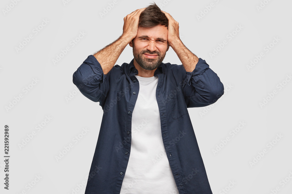 People and problems concept. Desperate displeased unshaven Caucasian guy keeps hands on head, regrets about his wrong doing or action, dressed in casual clothes, isolated over white studio wall. People and problems concept. Desperate displeased unshaven Caucasian guy keeps hands on head, regrets about his wrong doing or action, dressed in casual clothes, isolated over white studio wall.