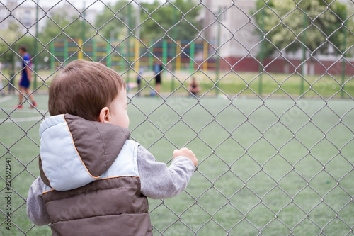 A boy 1,5 years old at the edge of a stadium watching football
