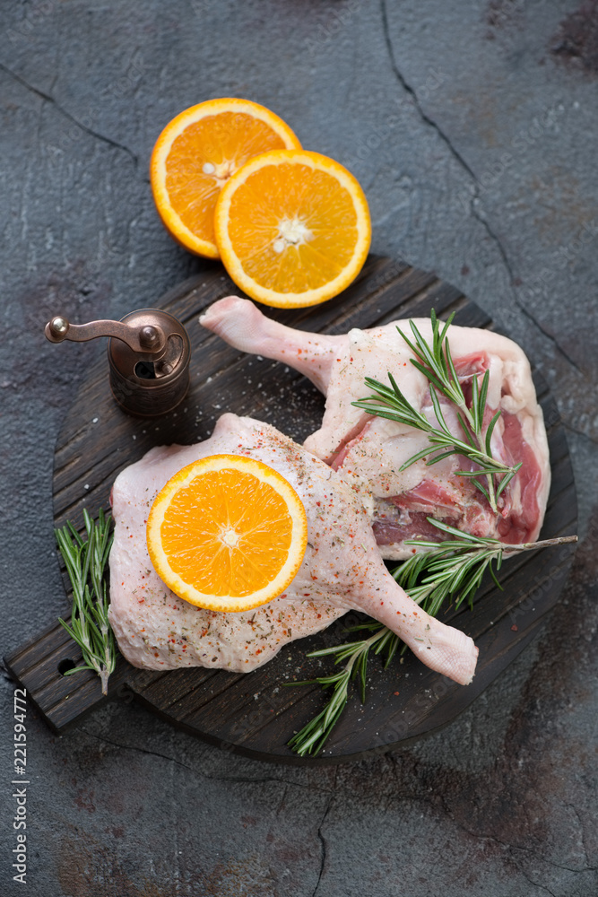 Fresh uncooked duck legs with orange slices and rosemary, high angle