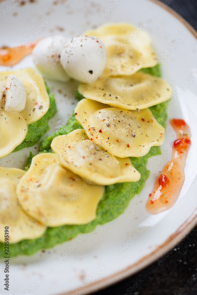 Close-up of ravioli on a bedding of green peas puree, vertical shot, selective focus Close-up of ravioli on a bedding of green peas puree, vertical shot, selective focus