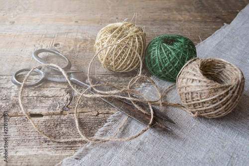 Three brown and green thread ball with antique vintage scissors on textured old wooden boards. Rustic, wabi sabi needlework, hobby, sewing and tailoring