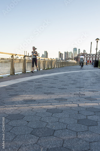 Woman jogging along East River under in New York City with partial skyline view of Brooklyn and Manhattan in background