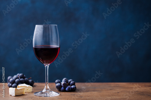 Glass of red wine with fresh grape and cheese on wooden table. Blue background. Copy space.