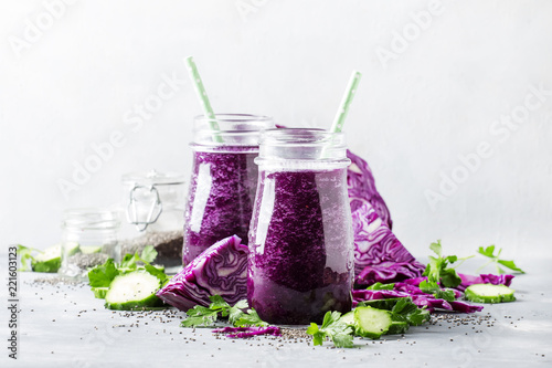 Vegan vegetable smoothie with purple cabbage, cucumber and chia seeds in glass bottles on gray table, selective focus