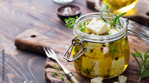 Feta cheese marinated in olive oil with fresh herbs in glass jar. Wooden background. Copy space.