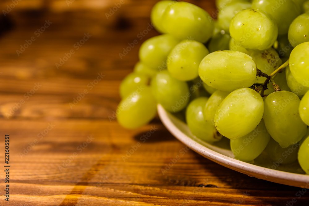 Ceramic plate with green grapes on wooden table Ceramic plate with green grapes on wooden table