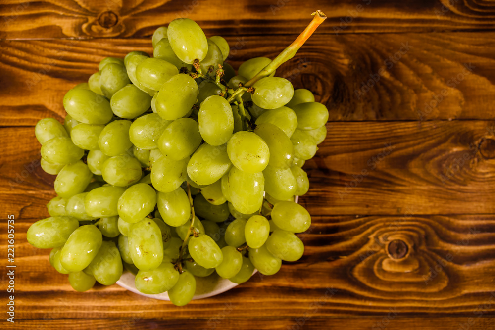 Ceramic plate with green grapes on wooden table. Top view Ceramic plate with green grapes on wooden table. Top view