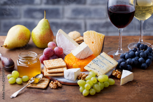 Assortment of cheese, grapes with red wine in glasses. Stone and wood background.