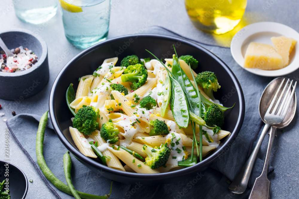 Pasta with green vegetables and creamy sauce in black bowl on grey stone background. Pasta with green vegetables and creamy sauce in black bowl on grey stone background.