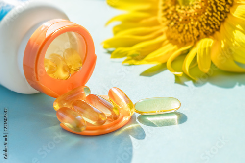 Canvas Print Golden Sunscreen pills with bottle and sunflower on blue background in sunlight