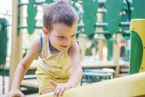 Little kid on a playground. Child playing outdoors in summer. Kids play on school yard. Happy kid in kindergarten or preschool. The boyis riding on a swing photo