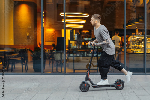 Attractive man riding a kick scooter at cityscape background.