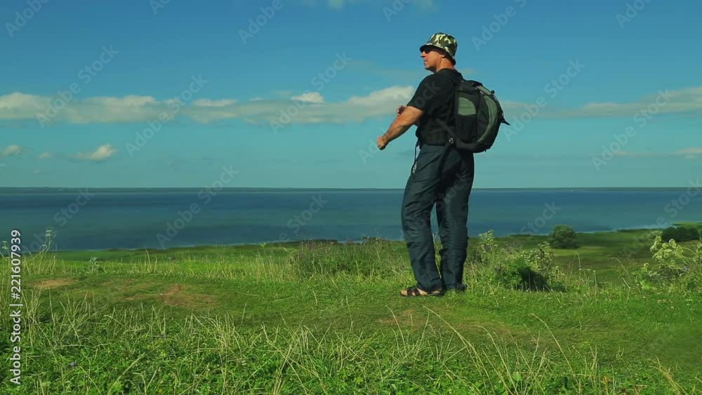 a man with a backpack behind him comes to the edge of the mountain and admires the view of the lake. shooting from the back. a man with a backpack behind him comes to the edge of the mountain and admires the view of the lake. shooting from the back.