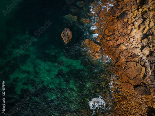 Aerial view of waves, rocks and transparent sea. Summer seascape. Top view from drone. Rocky coastline. 