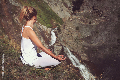 Woman in yoga positiion looks at waterfall photo