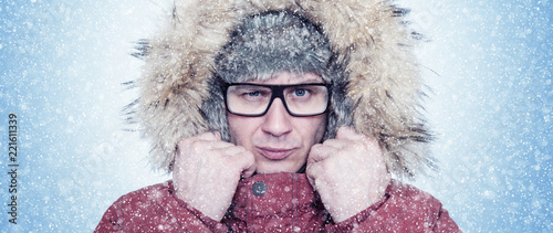 Portrait frozen man with glasses, winter clothes and a fur hat, cold, snow, blizzard 