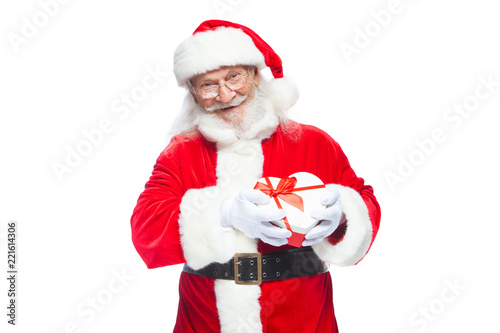 Christmas. Smiling Santa Claus in white gloves holds a red and white heart-shaped gift box with a red ribbon. Isolated on white background.