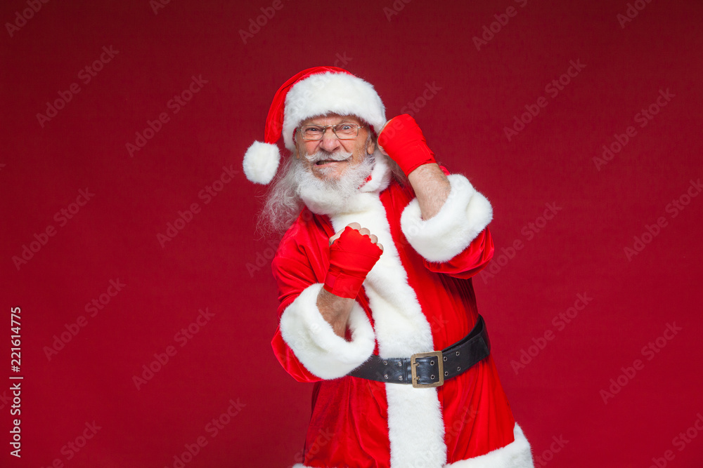 Christmas. Santa Claus with red bandages wound on his hands for boxing imitates kicks. Kickboxing, karate, boxing. Isolated on red background. Christmas. Santa Claus with red bandages wound on his hands for boxing imitates kicks. Kickboxing, karate, boxing. Isolated on red background.
