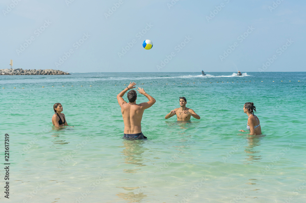 Four young fun people are playing volleyball on the beach at the coast of Dubai. Positive human emotions, feelings, joy. Funny cute child making vacations and enjoying summer.