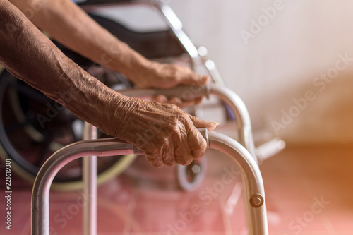 Asian old woman standing with her hands on a walker stand,Hand of patient woman holding a walking aid photo