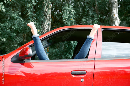 young woman driver resting in a red car, put her feet on the car window, happy travel concept