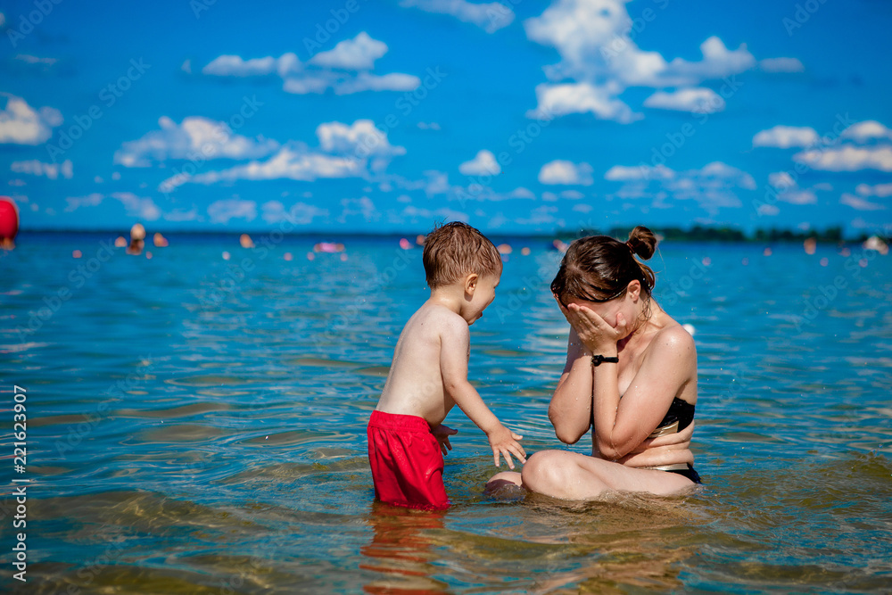 young mother with a little boy playing with water on the lake in the summer, family happiness, country family rest, summer warm day, happiness