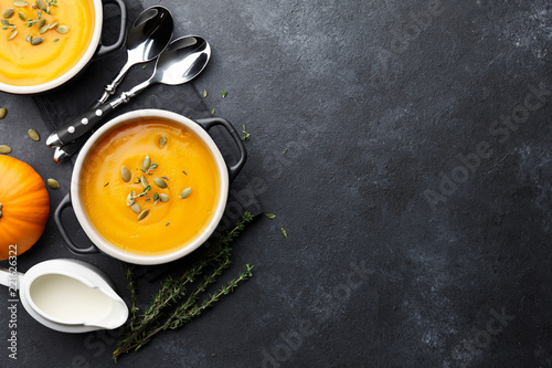 Pumpkin soup with thyme herb, cream and pumpkin seeds served in black bowl, top view