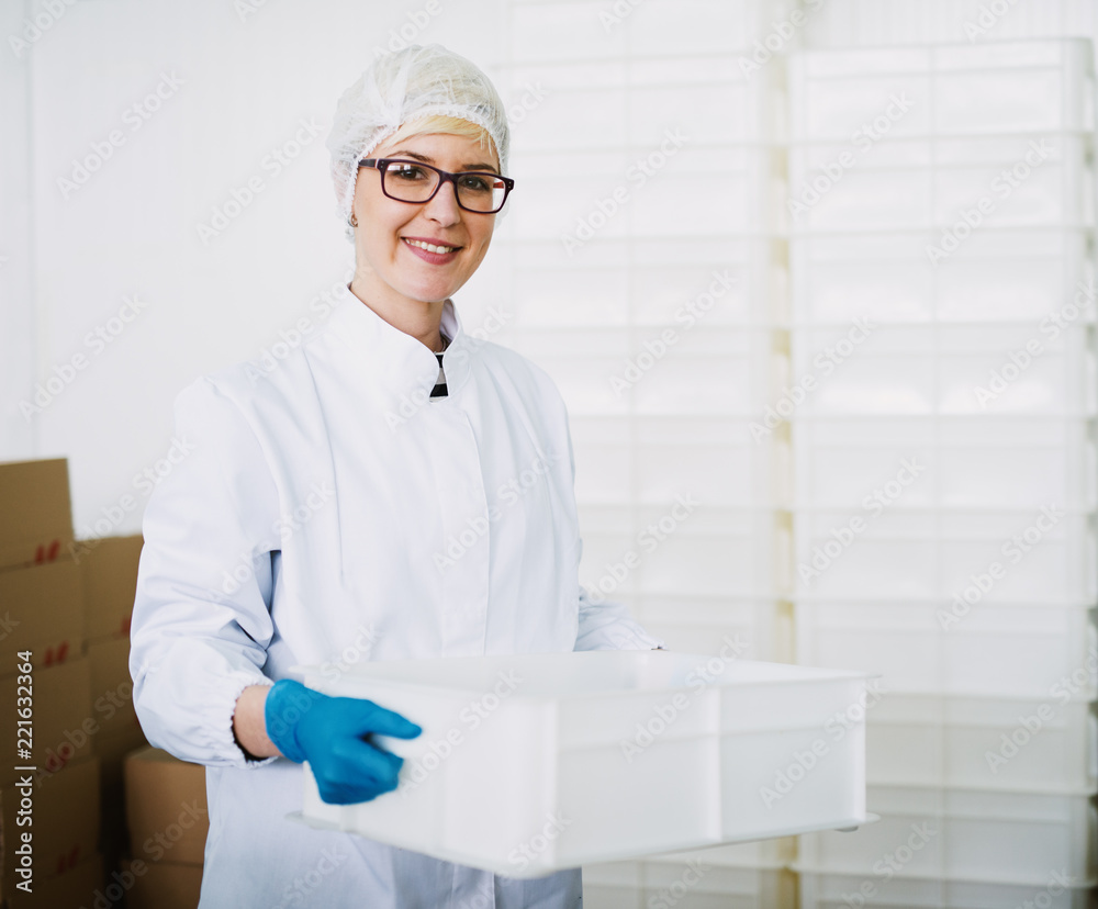 Smiley female worker in sterile clothes is putting away a plastic box . Smiley female worker in sterile clothes is putting away a plastic box .