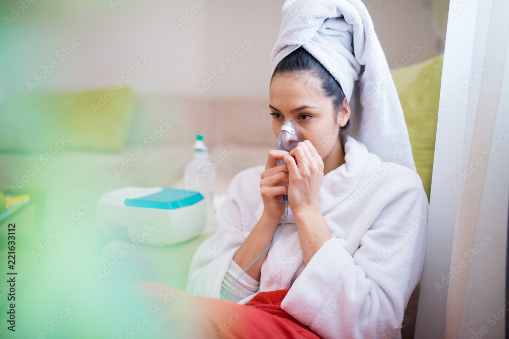 Young beautiful and exhausted female is using the inhaler on her sofa. Young beautiful and exhausted female is using the inhaler on her sofa.