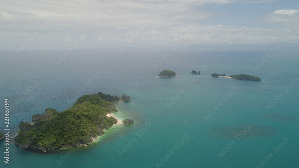 Aerial view of island Kagbalinad with sand beach and turquoise water in blue lagoon among coral reefs, Caramoan Islands, Philippines. Mountains covered with tropical forest.