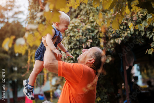 Love on first sight. Proud grandfather playing with is grandson in a backyard, lifting him in the air.