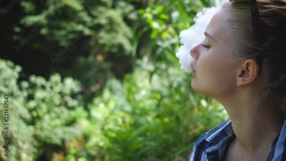 Young beautiful woman smoking (vaping) e-cigarette with smoke outdoors Young beautiful woman smoking (vaping) e-cigarette with smoke outdoors