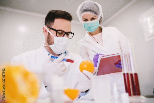 Employees in a lab taking a sample from orange with syringe.