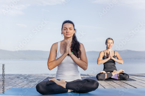 Young attractive smiling women practicing yoga on a lake