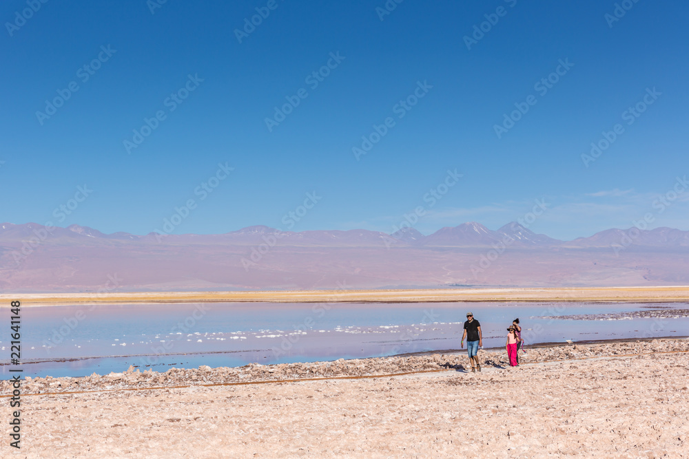 Atacama, Chile - Oct 9th 2017 - Parent and a child walking on the edge of the salt flat of Atacama in a pale light, afternoon, volcano in the background, Chile.