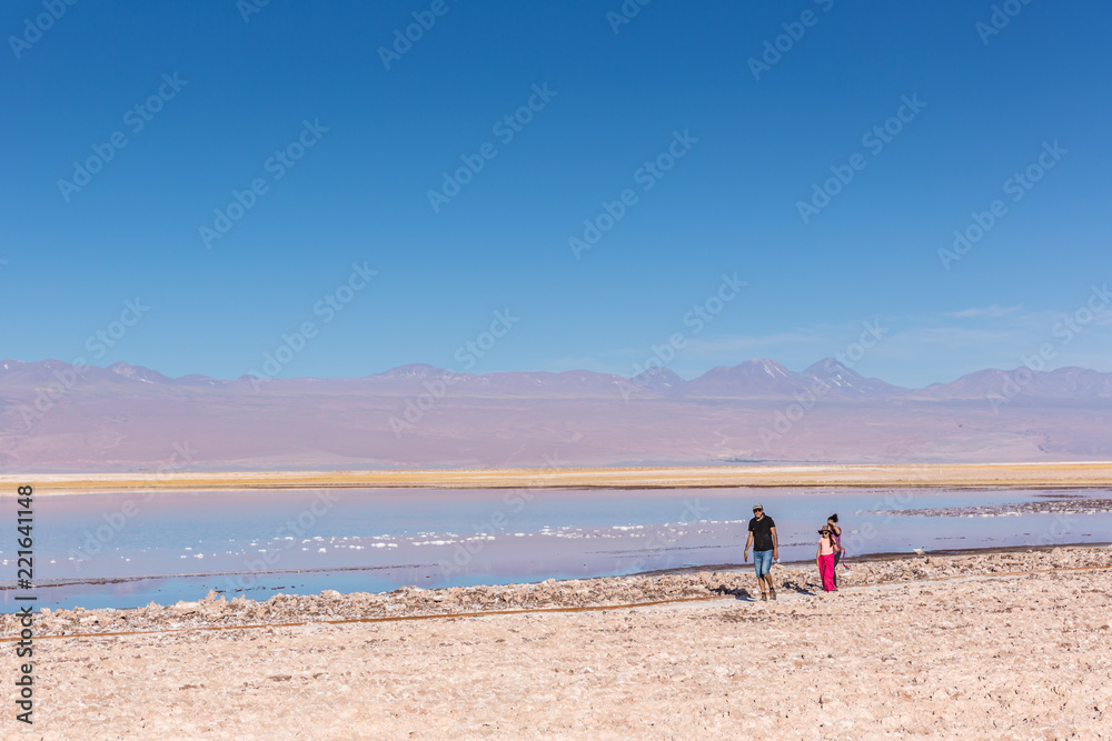 Atacama, Chile - Oct 9th 2017 - Parent and a child walking on the edge of the salt flat of Atacama in a pale light, afternoon, volcano in the background, Chile. Atacama, Chile - Oct 9th 2017 - Parent and a child walking on the edge of the salt flat of Atacama in a pale light, afternoon, volcano in the background, Chile.