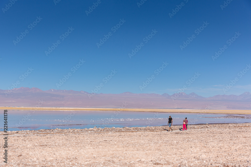 Atacama, Chile - Oct 9th 2017 - Wide angle shot of parent and a child walking on the edge of the salt flat of Atacama in a pale light, afternoon, volcano in the background, Chile.