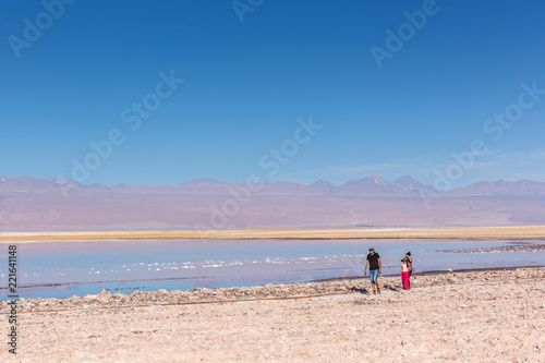Atacama, Chile - Oct 9th 2017 - Parent and a child walking on the edge of the salt flat of Atacama in a pale light, afternoon, volcano in the background, Chile.