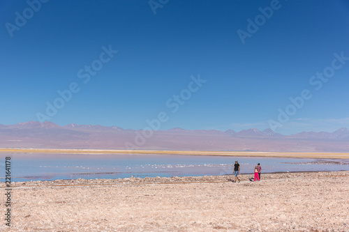 Atacama, Chile - Oct 9th 2017 - Wide angle shot of parent and a child walking on the edge of the salt flat of Atacama in a pale light, afternoon, volcano in the background, Chile.