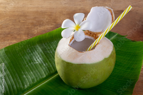 Green coconut fruit cut open to drink juice and eat. Flat lay on green banana leaf and wood background.