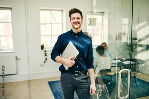 Smiling young businessman standing with his laptop in an office photo