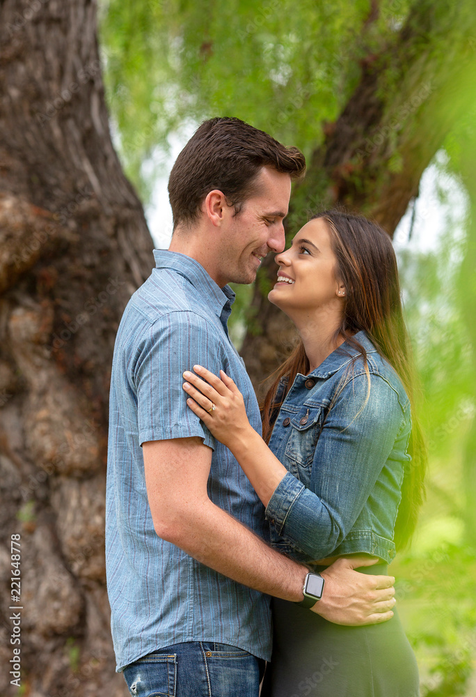 Young attractive happy couple smiling and looking at each other under a tree Young attractive happy couple smiling and looking at each other under a tree