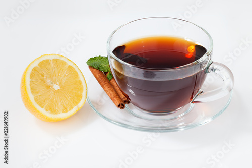 A glass cup with black tea on a saucer with mint, cinnamon, as well as lemon