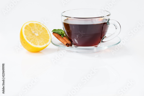 A glass cup with black tea on a saucer with mint, cinnamon, as well as lemon
