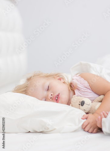 little baby girl sleeping on a bed with toy bear