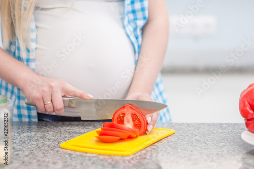 Close up pregnant woman with knife on kitchen cuts tomato